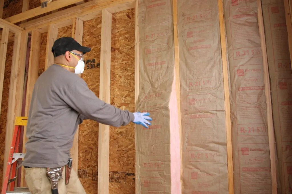 Insulation contractor installing fiberglass batt insulation in an unfinished wall.
