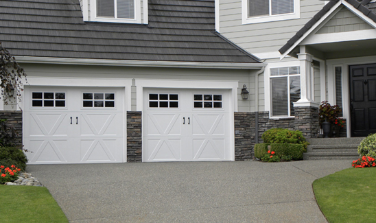 White carriage-style double garage doors on large home with light gray siding.