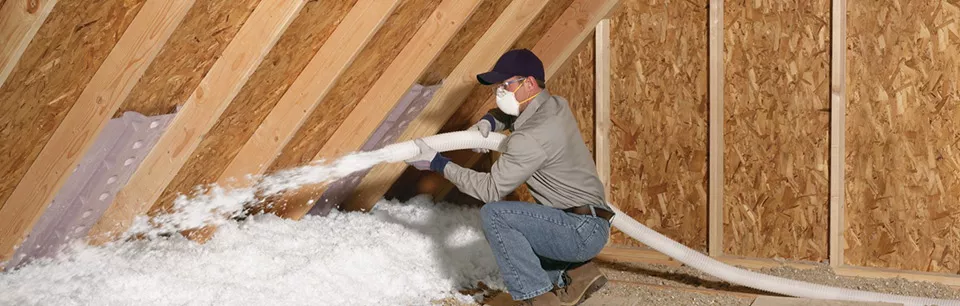 A technician installing blown-in insulation in an attic